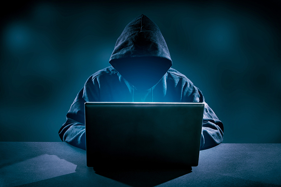 haker siedzący w kapturze w ciemnym pomieszczeniu na laptopie