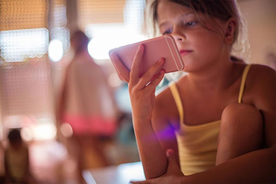 mała dziewczyna siedzi trzymając telefon w ręce i patrząc w ekran