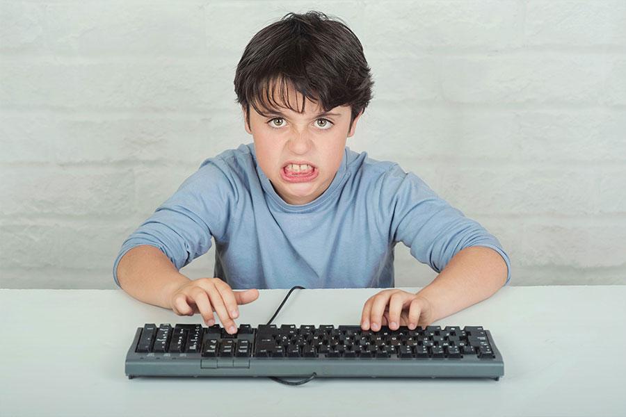 wkurzony mały chłopak w niebieskiej koszulce siedzi naciskając na klawiaturę
