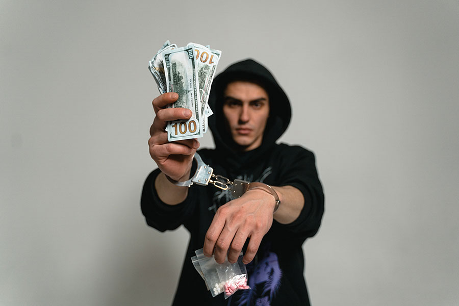 osoba w kajdanach trzyma dollary i narkotyki w rękach