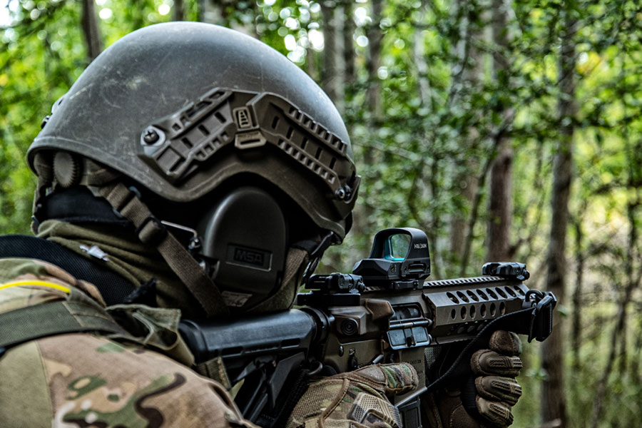Żołnierz w lesie z bronią patrzy przez kolimator