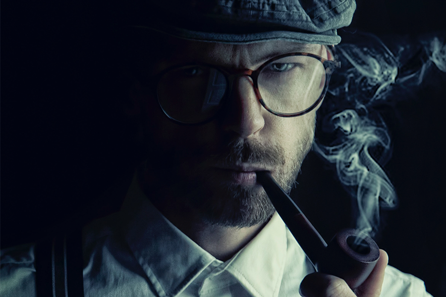 Detektyw w okularach w czapce pali fajkę