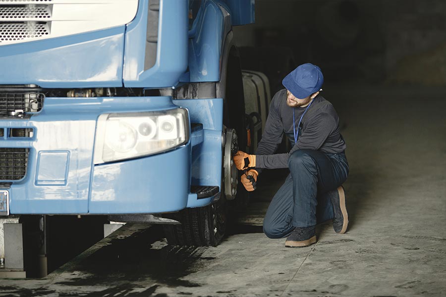 mężczyzna naprawia koło niebieskiej ciężarówki
