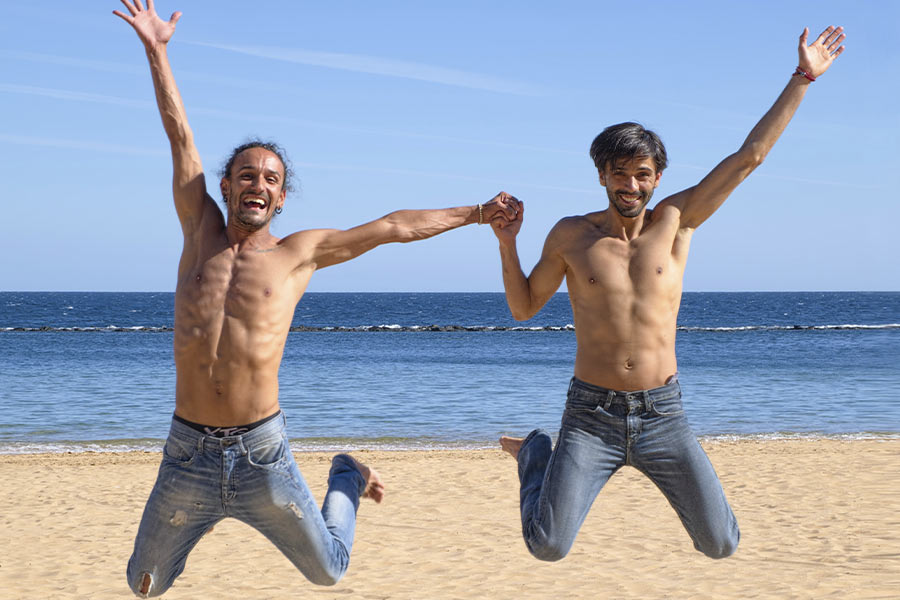 mężczyźni na plaży uśmiechnięci trzymają się za ręce