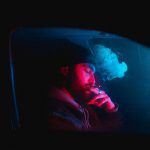 palący mężczyzna siedzi i pali marihuanę w samochodzie