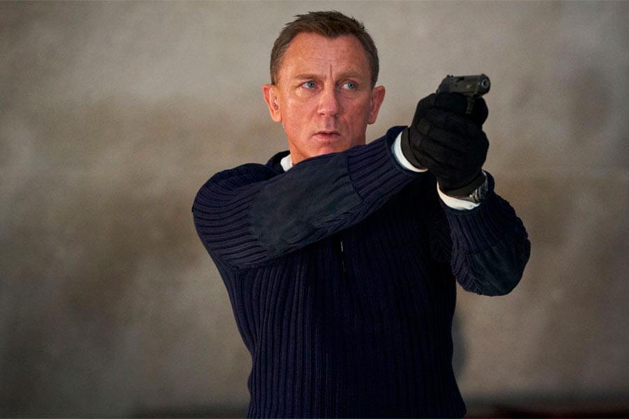 Daniel Craig stoi w ciemnym ubraniu trzymając pistolet przed sobą