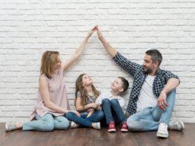 Rodzina zastępcza siedzi na podłodze: adoptowane dzieci między rodzicami. Para symbolicznie składa ręce w dach nad głowami pociech