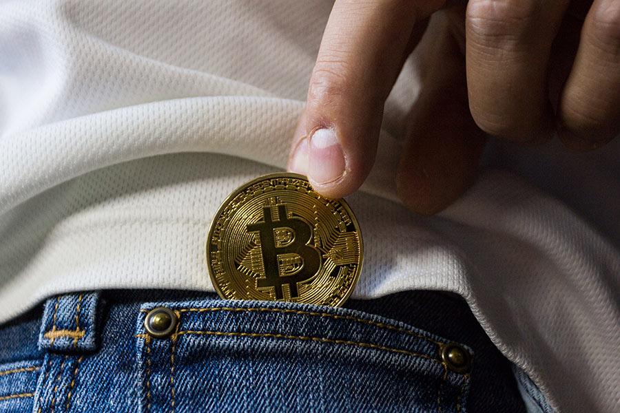 złota moneta bitcoin wyciąga się z kieszeni