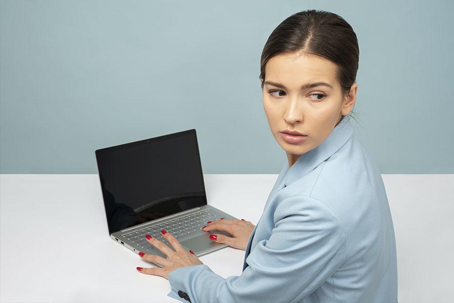 kobieta w niebieskiej koszulce siedzi odwrócona przed laptopem