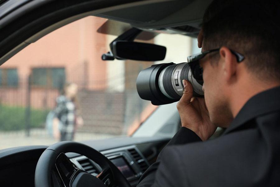 detektyw trzyma aparat i robi zdjęcia siedząc w samochodzie