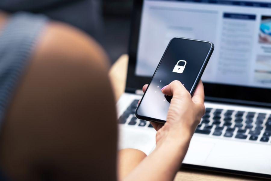 kobieta siedząc przed komputerem trzyma zablokowany telefon w ręce