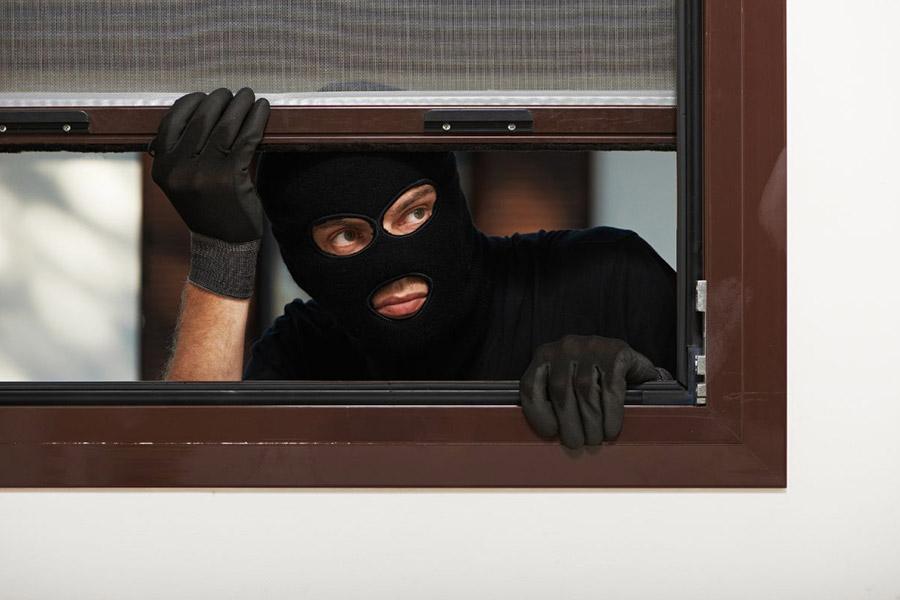 złodziej w czarnej masce i rękawicach próbuję dostać się do domu poprzez okno