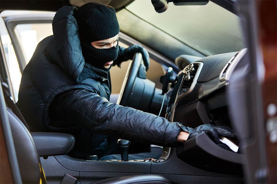 złodziej w czarnej masce siedzi za kierownicą i szuka czegoś w porwanym samochodzie