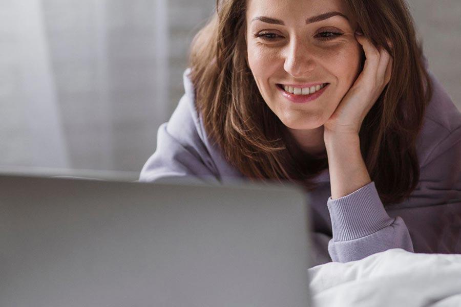 kobieta uśmiechnięta siedzi przed laptopem i opiera się o rękę