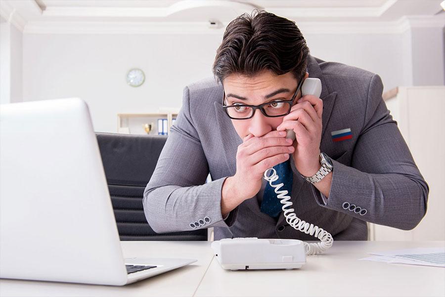 mężczyzna w garniturze siedząc w biurze przy laptopie po cichu rozmawia przez telefon