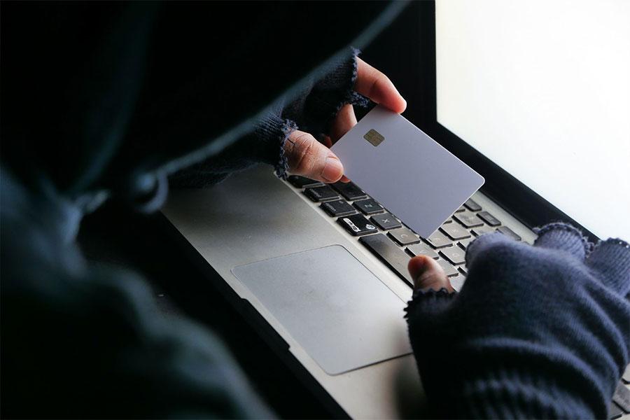 oszust siedzi przy laptopie z kartą płatniczą w ręce