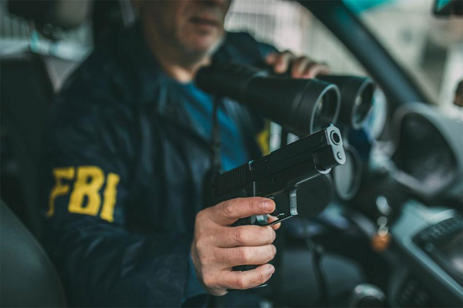 pracownik fbi siedzi za kierownicą z lornetką i pistoletem
