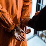 więzień w pomarańczowym ubraniu stoi plecami z kajdankami na rękach