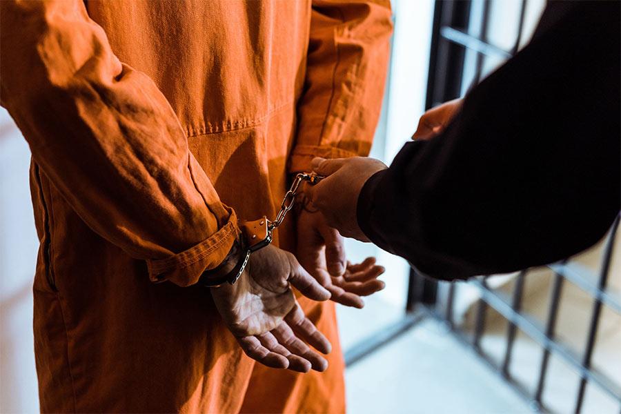 więzień w pomarańczowym ubraniu stoi plecami z kajdankami na rękach