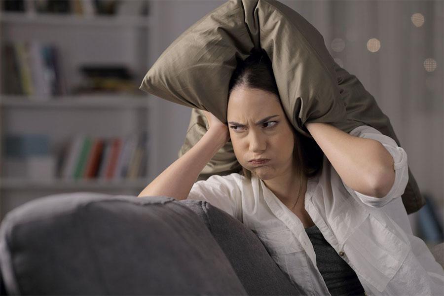 kobieta siedzi na kanapie zamykając uszy poduszkami