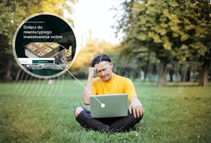 Zamyślony mężczyzna siedzi na trawie w parku. Na kolanach ma laptopa. Patrzy w niego, myśląc o fałszywych inwestycjach.