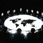 mężczyźni w białych maskach i garniturach siedzą dookoła stołu z mapą świata
