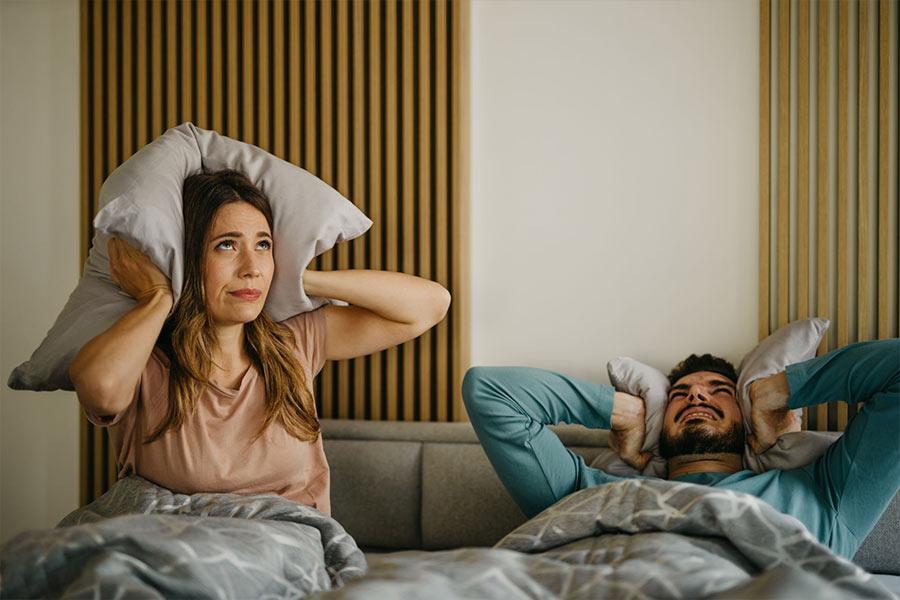 para mąż i żona leży w łóżku zamykając uszy poduszkami