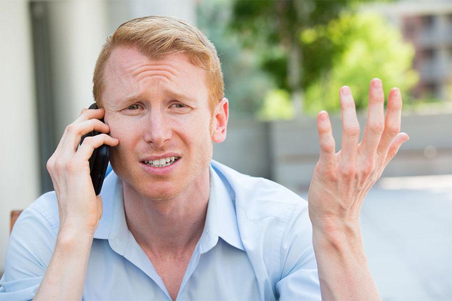 rudy rozczarowany mężczyzna siedzi na dworze i rozmawia przez telefon