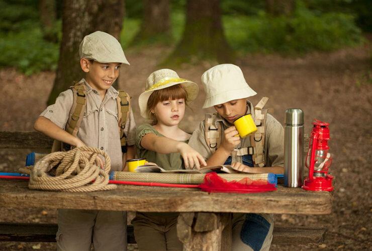 dzieci siedzą w lesie przy stole i coś oglądają