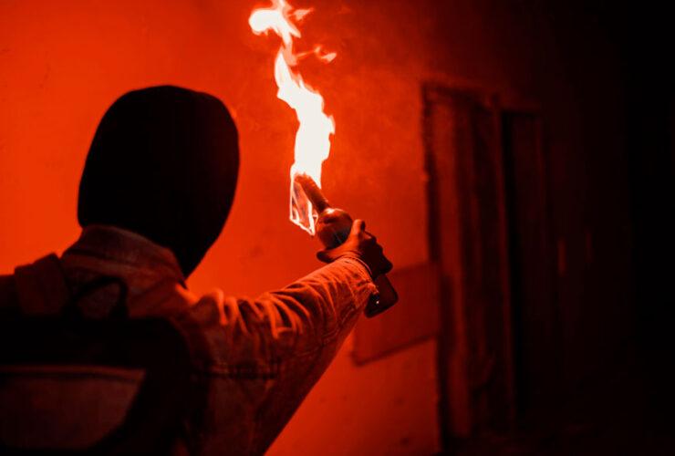 Anarchista w kapturze trzyma koktajl Mołotowa, by rzucić nim w budynek