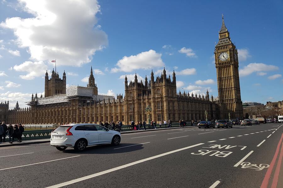 Biały samochód jedzie ulicą Londynu. W tle stoi Big Ben
