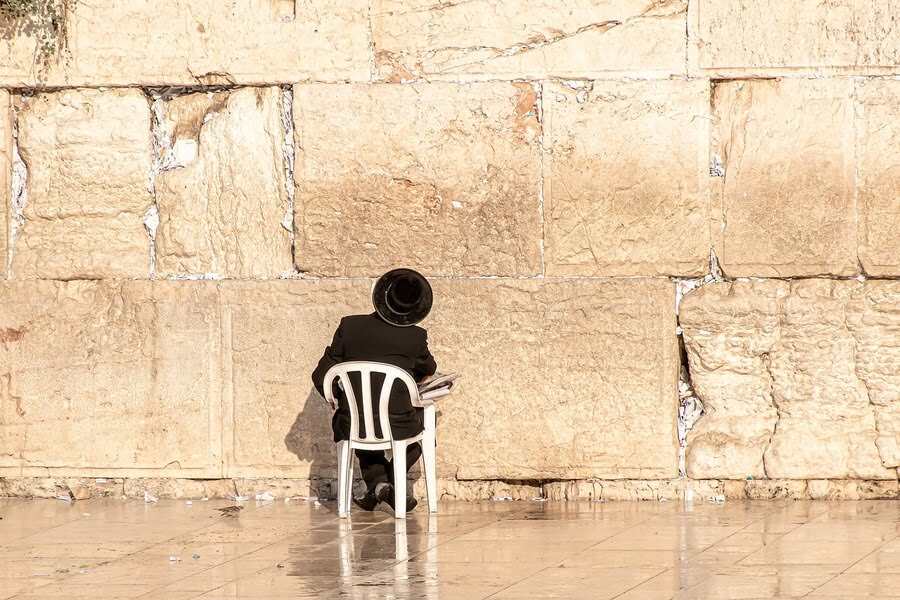 Żyd siedzi na plastikowym prześle przed Ścianą Płaczu