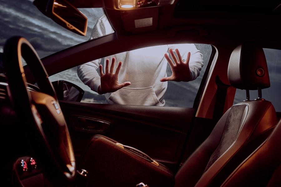 Mężczyzna w białej bluzie opiera się dłońmi na bocznej szybie samochodu