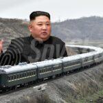 Pancerna lokomotywa sunie po torach. Zza niej wyłania się postać wodza Korei Północnej z uniesioną dłonią