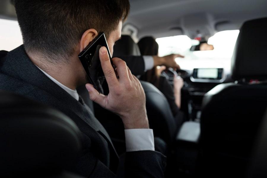 Mężczyzna na tylnym siedzeniu taksówki rozmawia przez telefon. Wskazuje kierowcy drogę.