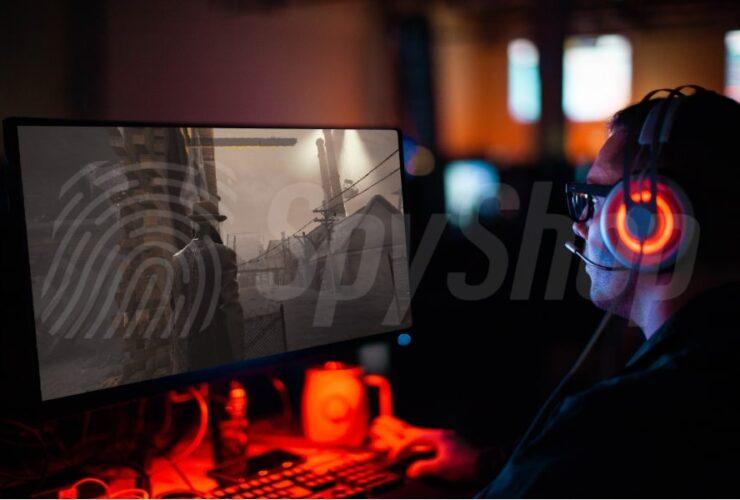 Mężczyzna w ciemności gra w grę komputerową. Na głowie ma świecące słuchawki. Na monitorze gra detektywistyczna.