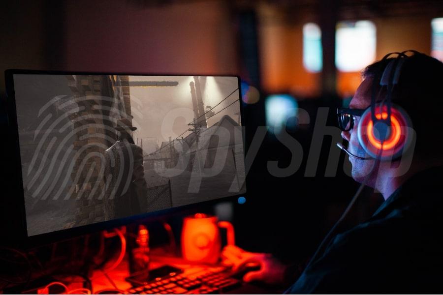 Mężczyzna w ciemności gra w grę komputerową. Na głowie ma świecące słuchawki. Na monitorze gra detektywistyczna.