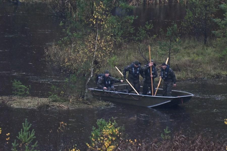 Po zarośniętym stawie pływa łódka. Czterech żołnierzy przeszukuje zbiornik za pomocą kijów.