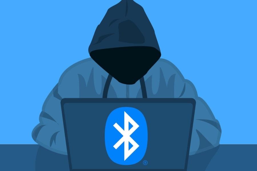 Grafika zakapturzonego hakera, który siedzi przed laptopem. Na laptopie logo Bluetooth.