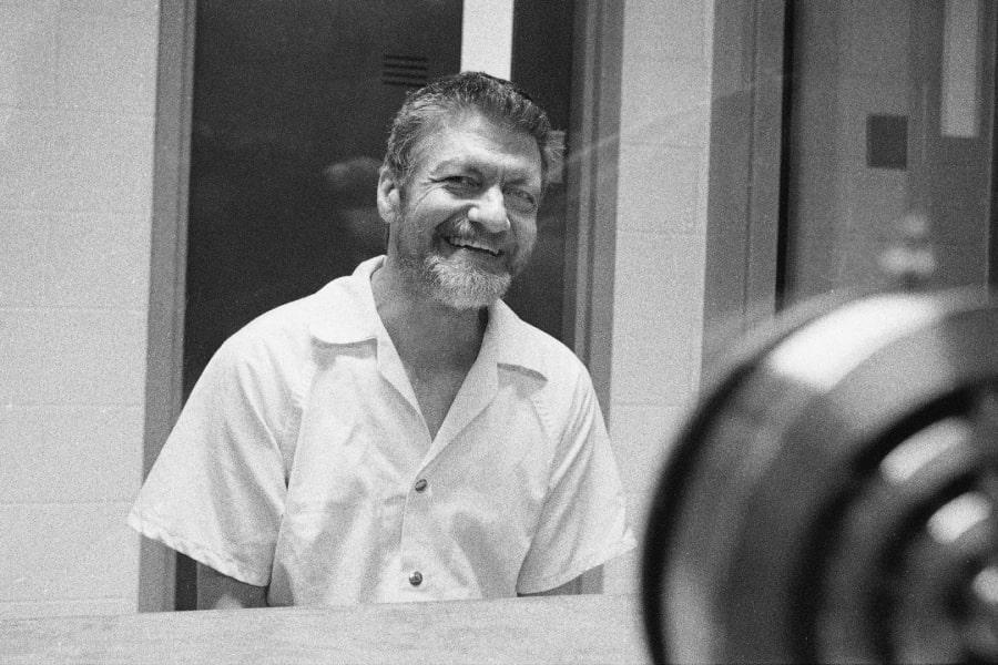 Czarnobiałe zdjęcie uśmiechniętego Teda Kaczynskiego na więziennym widzeniu.