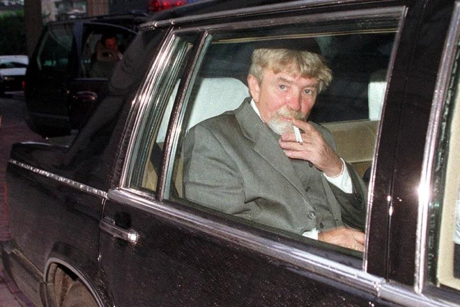 Zdjęcie Ryszarda Kuklińskiego, który pali papierosa siedząc na tylnej kanapie czarnej limuzyny.