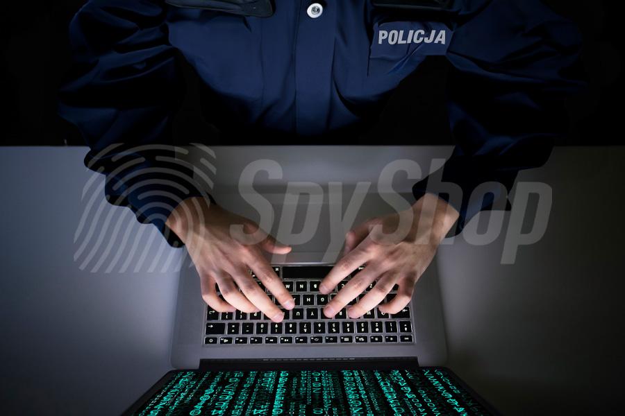Policjant w mundurze pracuje na laptopie i wydobywa dane z telefonu. Na ekranie widoczny transfer danych.