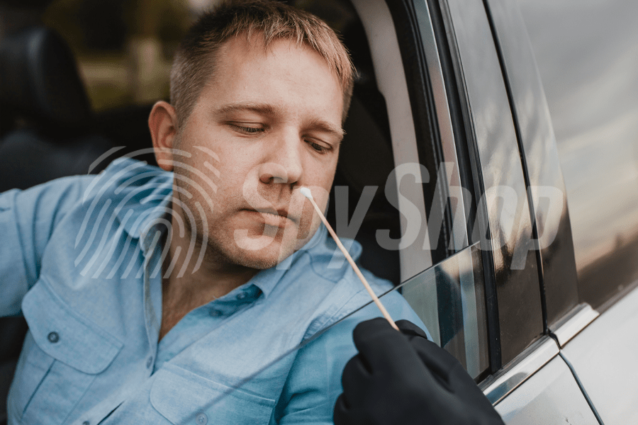 Zdjęcie przedstawiające kontrolę narkotykową u kierowcy. Dłoń policjanta w czarnej rękawiczce trzyma patyczek testowy, wyżej kierowca przygotowujący się do testu.