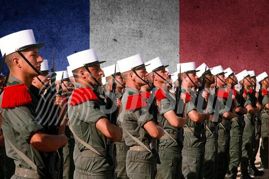 Zdjęcie szeregu żołnierzy Legii Cudzoziemskiej. W tle flaga Francji